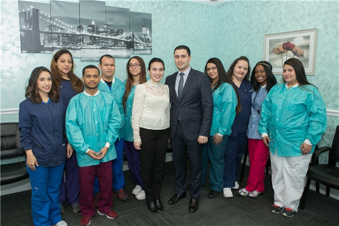 The image shows a group of people, likely healthcare professionals based on their attire and the setting, posing for a photograph in what appears to be a professional or educational environment. They are standing behind a table with a picture frame on it, which suggests they may be at an event or celebration.