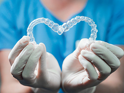 A dental professional s hand holding a transparent heart-shaped dental retainer, symbolizing love and care in the context of dental health.