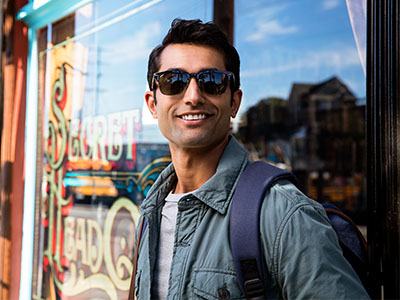 A man with sunglasses stands in front of a storefront, smiling at the camera.