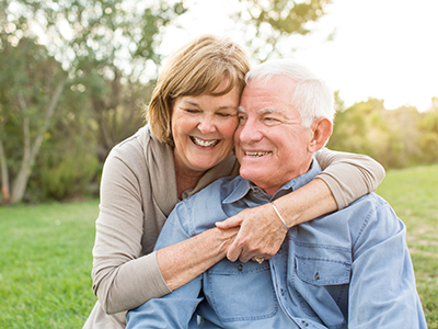 The image depicts an elderly couple sharing a warm embrace outdoors.