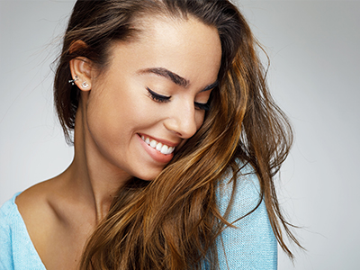 Smiling woman with long hair, wearing a light blue top, against a white background.